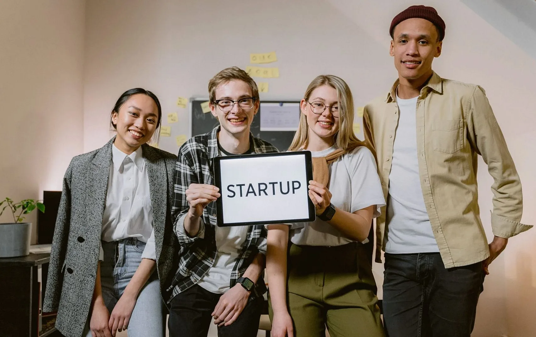 「STARTUP」と書かれたタブレットを持って並ぶ四人の若いチーム
